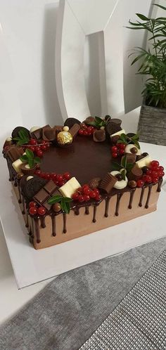 a heart shaped cake with chocolates and cherries on the top, surrounded by greenery