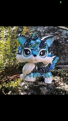 a blue and white cat figurine sitting on top of a rock next to plants