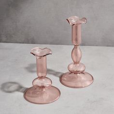 two pink glass candlesticks sitting on top of a white countertop next to each other