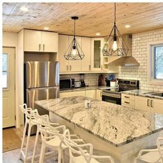 a kitchen with white cabinets and marble counter tops, an island in the middle is surrounded by chairs