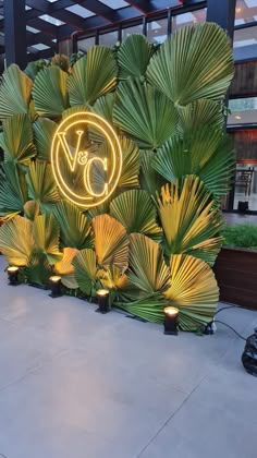 the neon sign is lit up in front of some plants and lights on the sidewalk