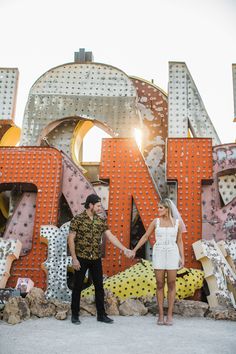 a man and woman holding hands standing in front of the neon sign for las vegas