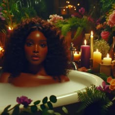 a woman sitting in a bathtub surrounded by candles and flowers with her hair pulled back