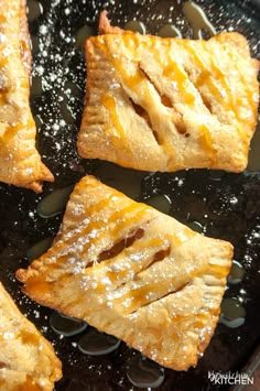 four pieces of pie sitting on top of a black pan covered in powdered sugar