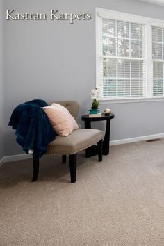 a chair and table in a room with carpeted floors, windows, and blinds