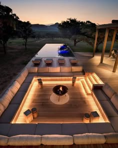 an outdoor living area with couches and tables lit up at night, overlooking a swimming pool