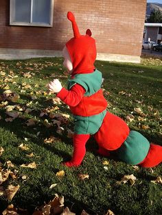 a small child in a red and green caterpillar costume running through the grass