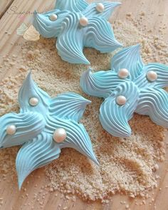 three blue decorated cookies sitting on top of a wooden table next to sand and shells