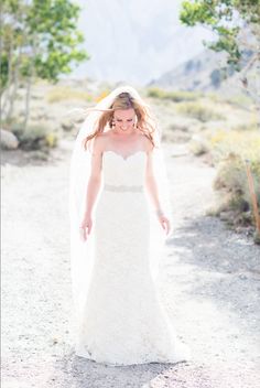 a woman in a wedding dress and veil walking down a dirt road