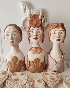 three ceramic heads with leaves on them are sitting next to other clay figures and plates