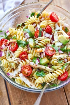 a glass bowl filled with pasta salad on top of a wooden table