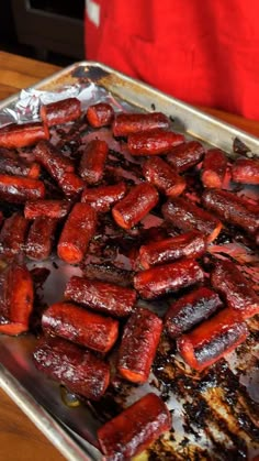 there is a pan full of cooked sausages on the table with someone's hand in the background