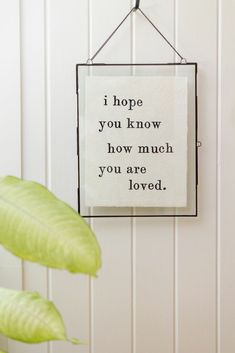 a sign hanging from the side of a white wall next to a green potted plant