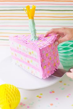 someone is decorating a cake with pink and yellow icing on the table next to some paper decorations