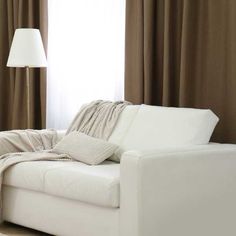 a white couch sitting in front of a window with curtains on both sides and a lamp next to it