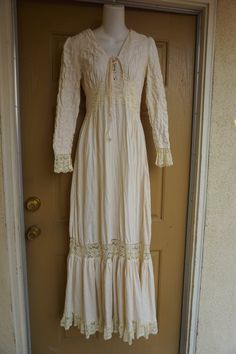 Size 13 Gunne Sax prairie dress fits smaller - please see measurements.  Zips in the back with adjustable tie at the back of the waist. Condition - has one small spot mid skirt to the side - see last photo.Measurements taken across front lying flat18" across front armpit to armpit14" across front of waist (ties tighter)59" length Bohemian Cream Maxi Dress For Fall, Bohemian Empire Waist Maxi Dress, Bohemian Empire Waist Fitted Maxi Dress, Bohemian Fitted Maxi Dress With Empire Waist, Bohemian Fitted Dress With Lace-up Back, Long Sleeve Lace Maxi Dress With Lace Trim, Bohemian Long Sleeve Prairie Dress With Ruffles, Fitted Bohemian Dress With Lace-up Back, Bohemian Prairie Dress With Ruffles And Long Sleeves