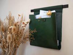 a green bag hanging on the wall next to dried flowers