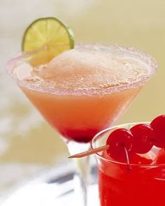 two cocktails sitting on top of a table next to each other with cherries