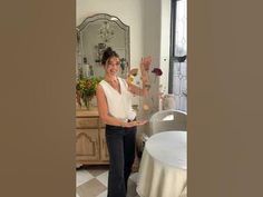 a woman standing in front of a table waving at the camera with her hands up