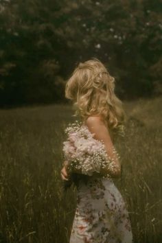 a woman in a floral dress standing in tall grass with her back to the camera