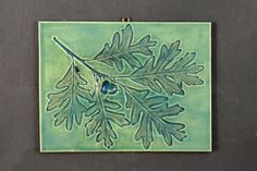 a ceramic tile with green leaves and blue beads on the bottom, hanging from a hook