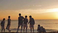 several people are standing on the beach watching the sun go down over the water and one person in striped shirt is holding a frisbee