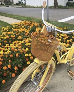 a yellow bicycle with a basket is parked on the side of the road next to some flowers