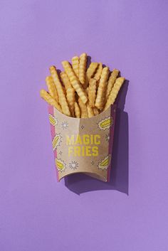 a paper container filled with fries on top of a purple surface and the words magic fries written in yellow