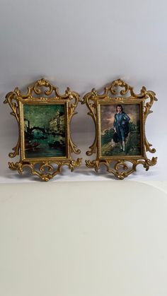 two gold framed pictures on a white surface