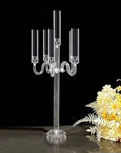 a glass candelabra with five candles on it and flowers in the background