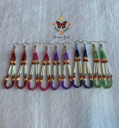 six pairs of multicolored beaded earrings are lined up on a white towel