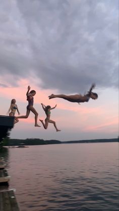 three people jumping into the water from a dock in front of a body of water