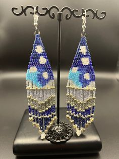 "Watch the clouds roll by over the mountains with this fun and sparkling earring. The bright blue sky and the deep blue waters are calming and full of life! Look at the little star on the fringe!  Silver-toned findings and glass seed beads - 5\" long" Blue Beaded Fringe Earrings For Festival, Blue Beaded Dangling Earrings For Festivals, Blue Beaded Earrings With Dangling Beads For Festival, Bohemian Blue Earrings With Beaded Fringe, Blue Dangling Beads Earrings For Festival, Artisan Blue Beaded Earrings As Gift, Blue Bohemian Beaded Fringe Earrings, Bohemian Blue Beaded Fringe Earrings, Adjustable Blue Beaded Fringe Earrings