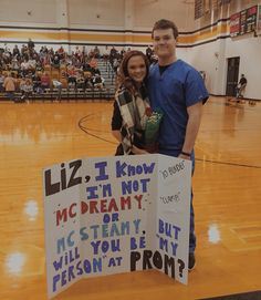 a man and woman standing next to each other in front of a sign on a basketball court