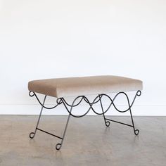 a bench sitting on top of a cement floor next to a white wall with a black iron frame