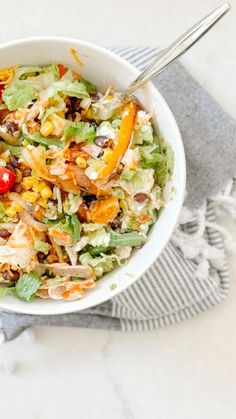 a white bowl filled with salad on top of a gray and white towel next to a fork