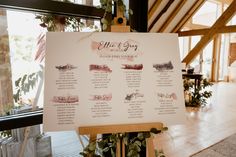 a wedding seating chart is displayed in front of a large window with greenery on it