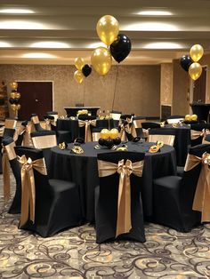 a banquet room with black tables and gold ribbons on the table, balloons in the air