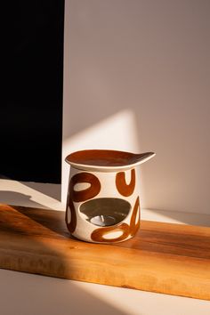 a white and brown cup sitting on top of a wooden table next to a computer monitor