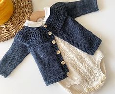 two knitted sweaters are next to a basket with an orange on the table