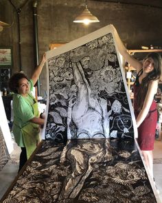 two women standing next to a large piece of art