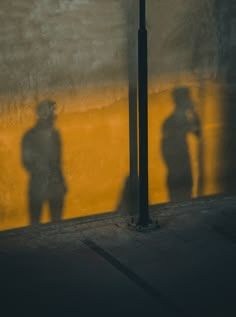 the shadow of two people standing in front of a street sign on a yellow wall