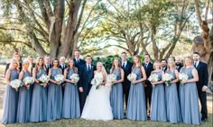 a bride and groom with their bridal party in front of trees at the park