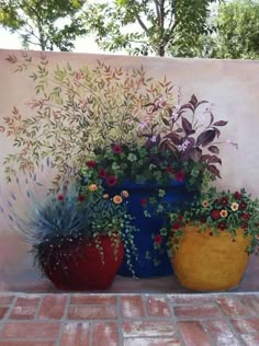 three large pots with flowers in them sitting on a brick floor next to a wall