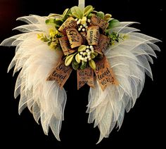 a wreath with white feathers and yellow flowers on the front of it, hanging from a door