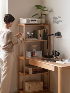 a woman standing in front of a book shelf next to a desk with a microwave on it