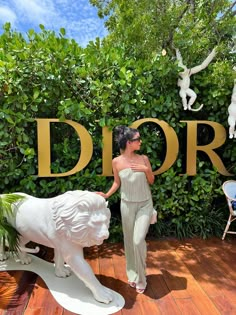 a woman standing next to a statue of a lion in front of a sign that says dior