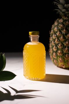 a pineapple sits next to a glass bottle