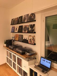 a laptop computer sitting on top of a wooden table next to a shelf filled with records