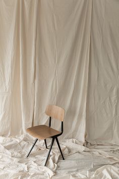 a wooden chair sitting on top of a white sheet covered floor next to a wall